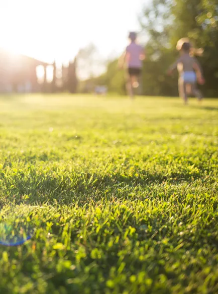 Children running across a sunlit green lawn